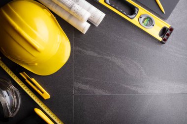 Müteahhit teması. Planlar, müteahhitin alet çantası, sarı başlık ve iftiralar. Gri karolar arka plan.