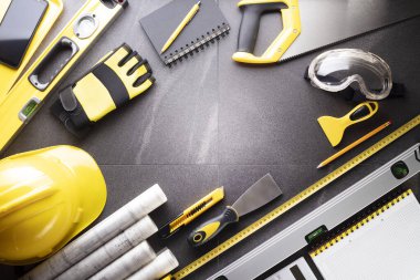 Müteahhit teması. Planlar, müteahhitin alet çantası, sarı başlık ve iftiralar. Gri karolar arka plan.