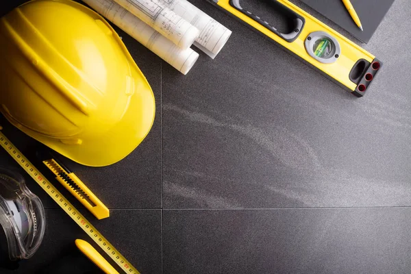 Müteahhit teması. Planlar, müteahhitin alet çantası, sarı başlık ve iftiralar. Gri karolar arka plan.