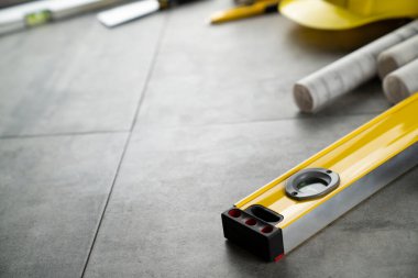 Müteahhit konsepti. Müteahhidin alet çantası, sarı başlık, libella, el testeresi. Gri karoların arka planındaki planlar ve defterler.