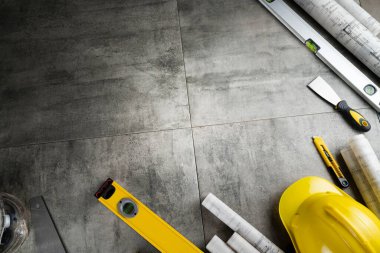 Müteahhit konsepti. Müteahhidin alet çantası, sarı başlık, libella, el testeresi. Gri karoların arka planındaki planlar ve defterler.