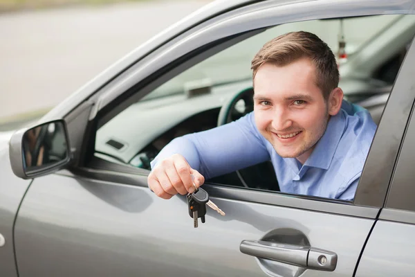 Un joven sentado dentro de un coche nuevo con llaves. Sonriendo. — Foto de Stock