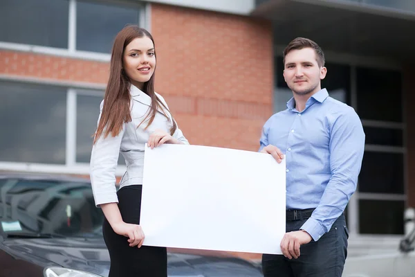 Mladý pár se drží bílý list na pozadí vozu — Stock fotografie