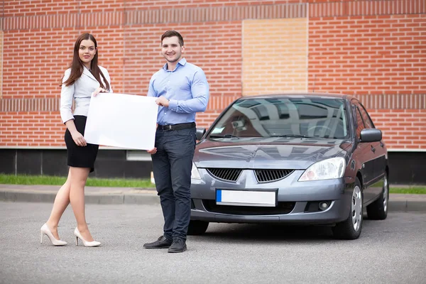 Pareja joven sosteniendo una sábana blanca sobre un fondo del coche — Foto de Stock