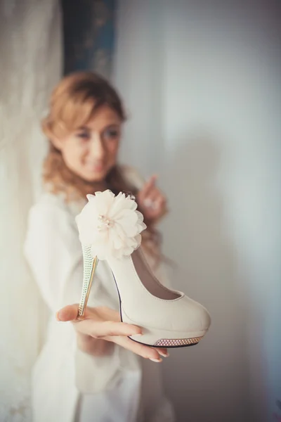 Belle mariée garde sur les chaussures de main dans sa chambre. Mariée du matin . — Photo