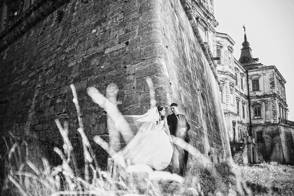 Hermosa novia morena abrazando novio y posando cerca del viejo castillo — Foto de Stock