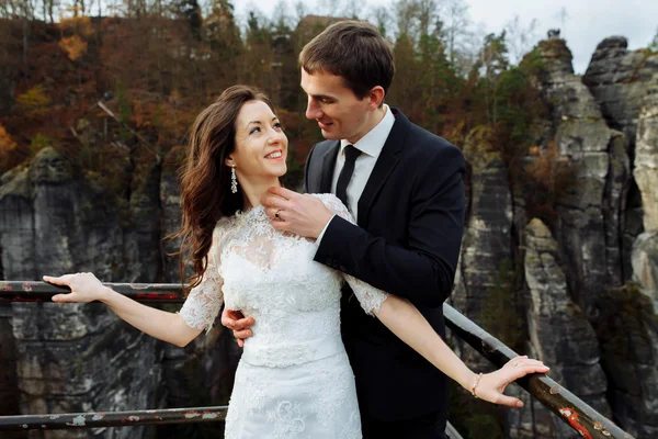Mariée heureuse de luxe et marié élégant baisers sur fond de vue des rochers ensoleillés dans les montagnes étonnantes — Photo
