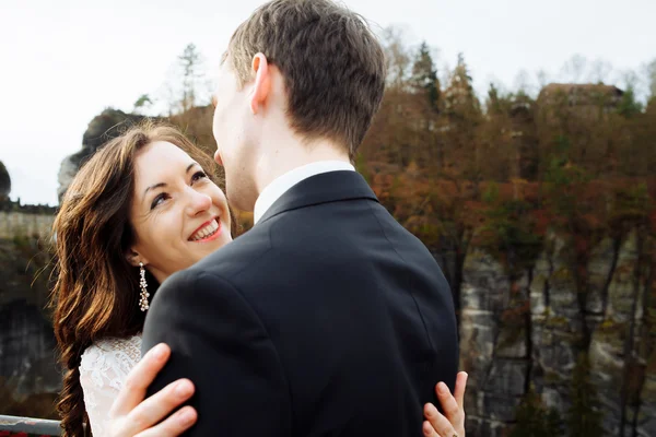 Mariée heureuse de luxe et marié élégant baisers sur fond de vue des rochers ensoleillés dans les montagnes étonnantes — Photo