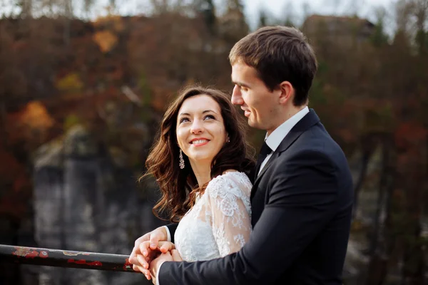 Luxury happy bride and stylish groom hugging each other with tender on background of sunny rocks in amazing mountains — Stock Photo, Image