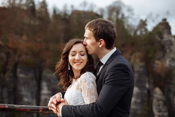 Mariée heureuse de luxe et marié élégant s'embrassant avec tendresse sur fond de rochers ensoleillés dans des montagnes étonnantes — Photo