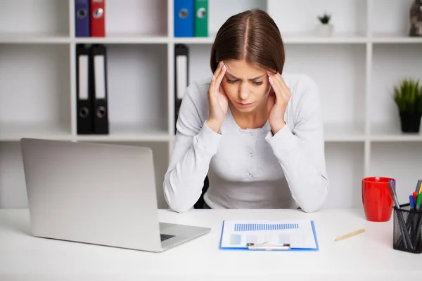 Kobieta pracująca w biurze przed laptopem cierpiąca na przewlekłe codzienne bóle głowy. — Zdjęcie stockowe