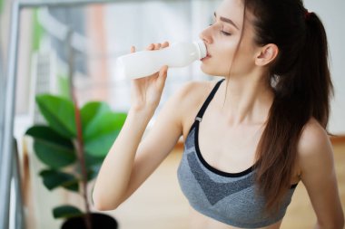 Genç ve güzel bir kadın plastik bir şişe yoğurttan içiyor.