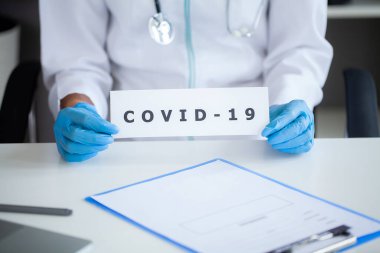 Octor elinde covid-19 yazılı kağıt bir kart tutuyor.