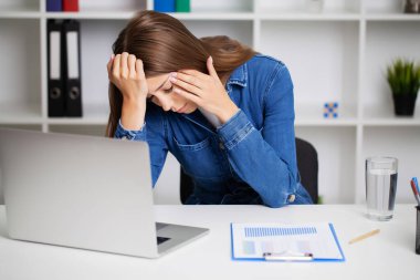 Ofis masasında çalışan bir kadın dizüstü bilgisayarın önünde günlük baş ağrısı çekiyor..