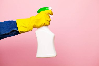 Sarı eldivenli bir el pembe arka planda bir temizlik sıvısı spreyi tutar..