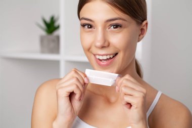 Diş beyazlatıcı, gülümseyen güzel bir kadın elinde beyaz bir şerit tutuyor..