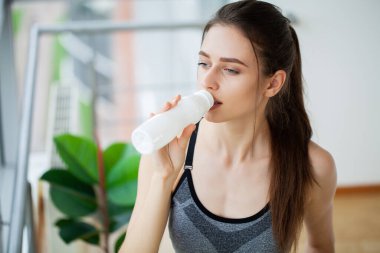 Genç ve güzel bir kadın plastik bir şişe yoğurttan içiyor.