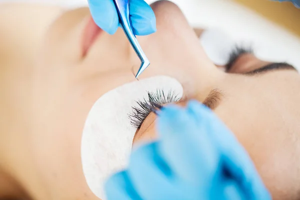 Close-up master of eyelash extensions extends eyelashes to a beautiful woman