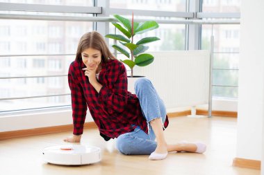 Yerleri temizlemek için otomatik süpürge kullanan genç bir kadın.