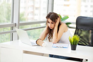 Ofis masasında çalışan ve dizüstü bilgisayarla yazan kendine güvenen genç bir iş kadını.