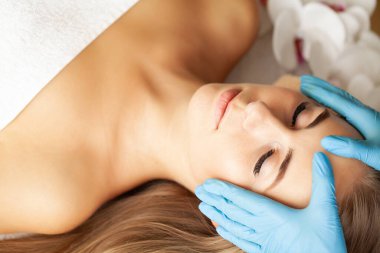 Genç ve güzel bir kadın yüz masajı yaptırıyor.