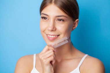 Diş beyazlatıcı, gülümseyen güzel bir kadın elinde beyaz bir şerit tutuyor..