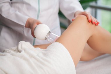 Kadın elektrikli süpürge kullanarak bacak masajı yaptırıyor.