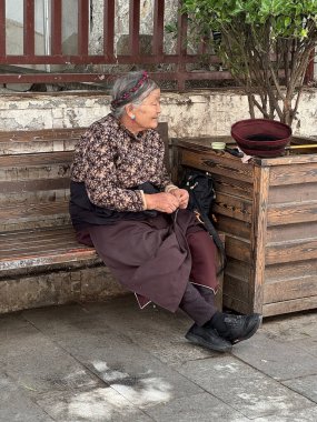 Yaşlı bir Tibetli kadın, Çin 'in Tibet, Lhasa kentinin caddesi boyunca uzanan bir bankta dinleniyor. Lhasa, Çin 'in Tibet Özerk Bölgesinin başkentidir..