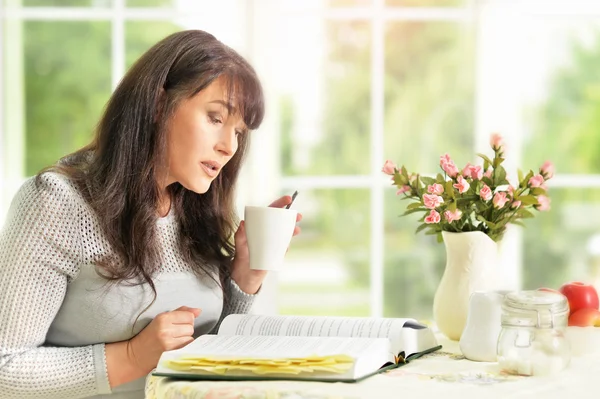 Mulher sênior lendo um livro com chá — Fotografia de Stock