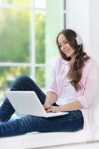 Jovem mulher em fones de ouvido com laptop — Fotografia de Stock