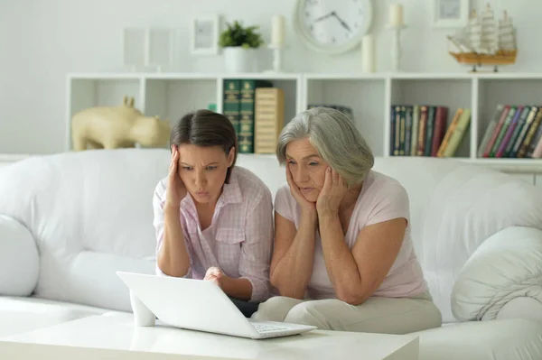 悲伤的母亲和女儿坐在桌旁 带着笔记本电脑 在家里 — 图库照片