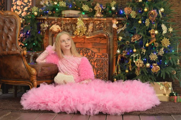 漂亮的女孩穿着粉红的衣服坐在圣诞树旁 — 图库照片