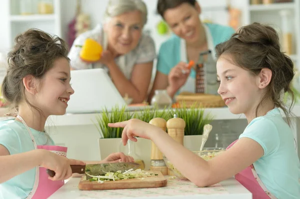 可愛いです女の子調理中おいしい新鮮なサラダを準備します 背景に母親と祖母 — ストック写真
