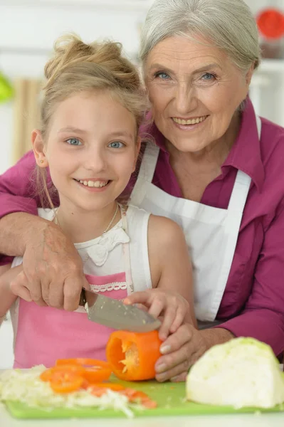 笑顔の先輩と孫娘がキッチンでサラダを作って — ストック写真