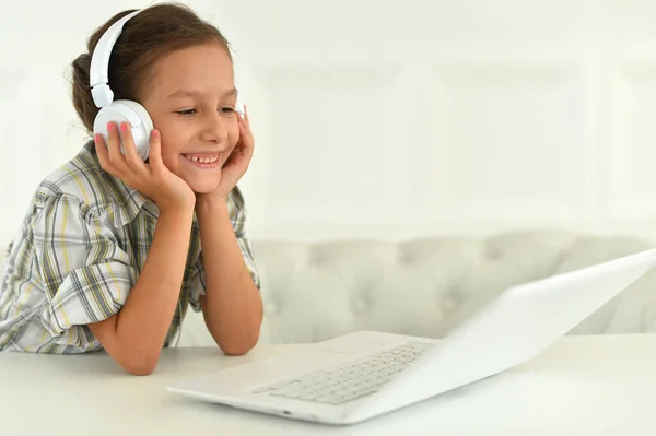 一个戴耳机的可爱女孩在家里书桌边用笔记本电脑 — 图库照片