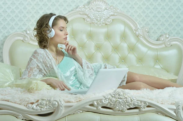 漂亮的年轻女子在家里抱着笔记本电脑躺在床上 — 图库照片