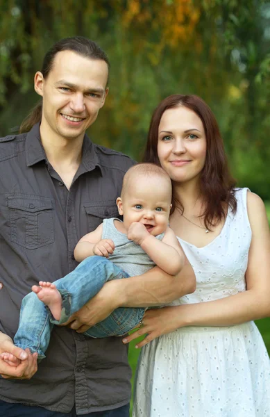 Família feliz segurando filho no parque — Fotografia de Stock