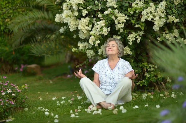 Äldre kvinna sitter under bush — Stockfoto