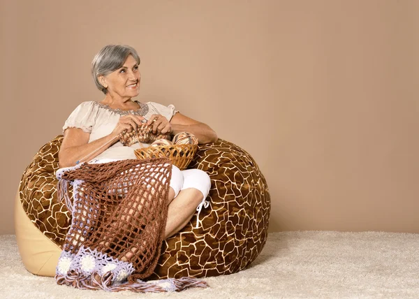 Senior woman knitting sitting in armchair — Stock Photo, Image