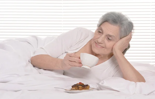 Donna anziana con torta in camera da letto — Foto Stock