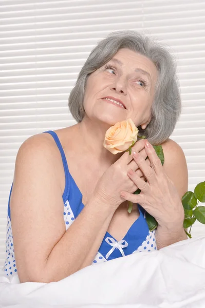 Mujer mayor en la cama con rosa — Foto de Stock