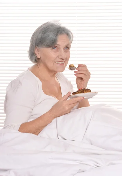 Mujer mayor en el dormitorio con pastel — Foto de Stock