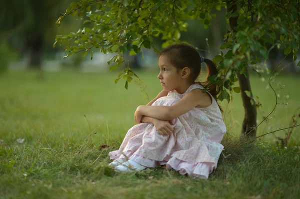 Klein meisje zit onder de boom — Stockfoto