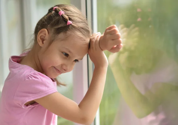 Liten flicka står nära fönster — Stockfoto