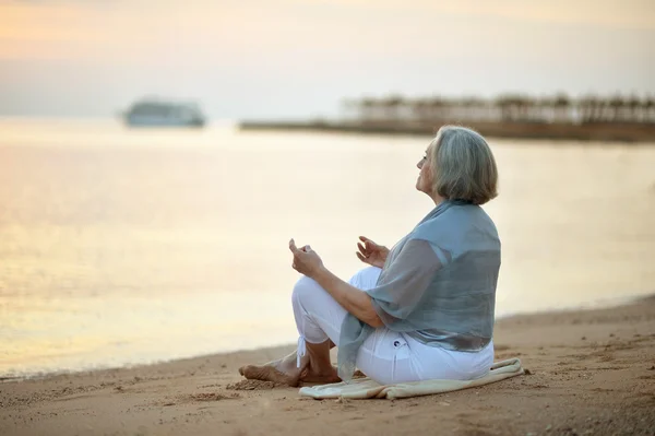 Mulher madura meditando na praia — Fotografia de Stock