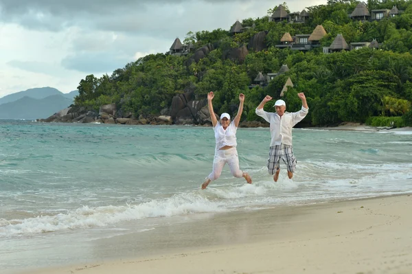 Bejaarde echtpaar springen op tropisch strand — Stockfoto