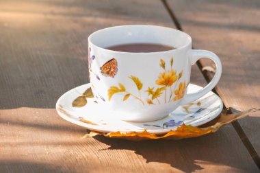 Ahşap bir masada servis edilen güzel boyanmış bir fincan ve aromatik çay.