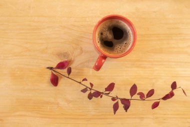 Ahşap bir masada sonbahar yapraklarıyla servis edilen kırmızı bir fincan koyu kahve.