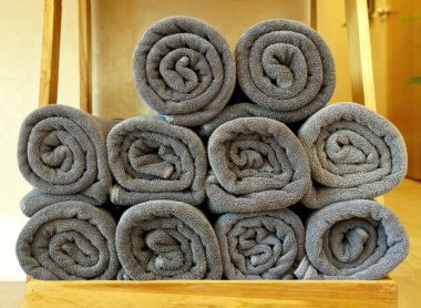 Rolls of gray towels are stacked on a wooden shelf.
