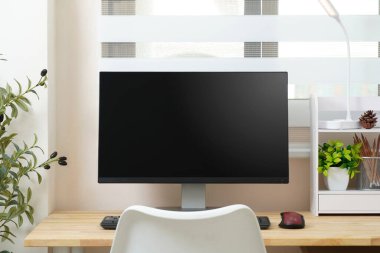 Asgari modern çalışma alanı, tahta masada bilgisayar monitörü, bitkilerle, klavyeyle, fareyle ve pencerenin sıcacık ve temiz tasarımıyla ev ofis kurulumu..